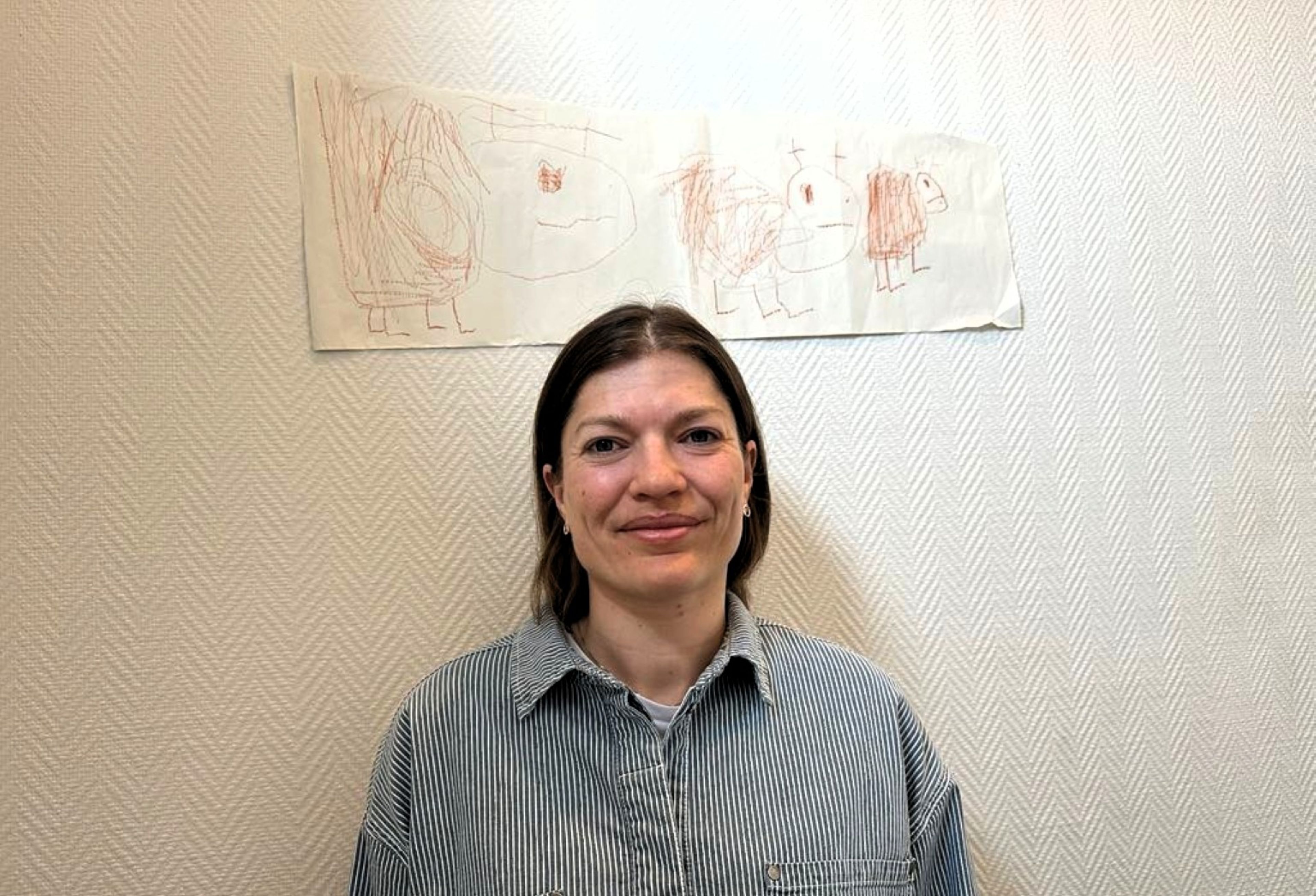Regine Bakken som smiler foran en vegg med tegninger på