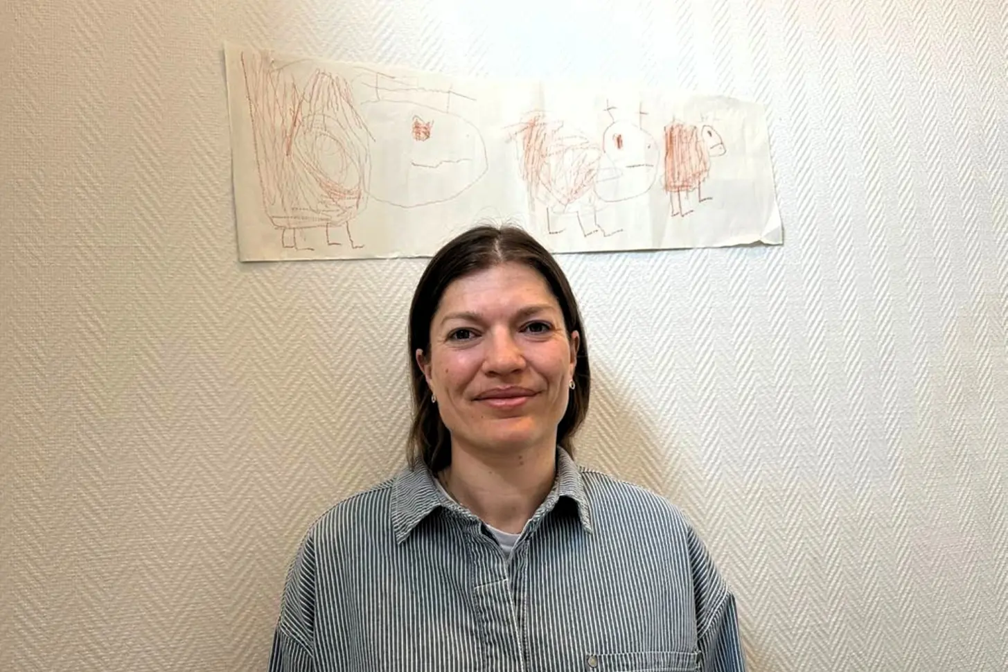Regine Bakken som smiler foran en vegg med tegninger på