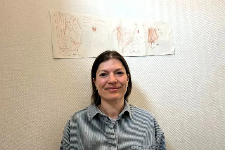 Regine Bakken som smiler foran en vegg med tegninger på