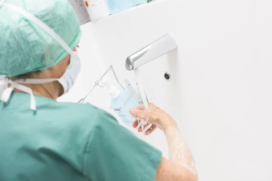 Ansatt kledd i grønt med munnbind vasker hendene.