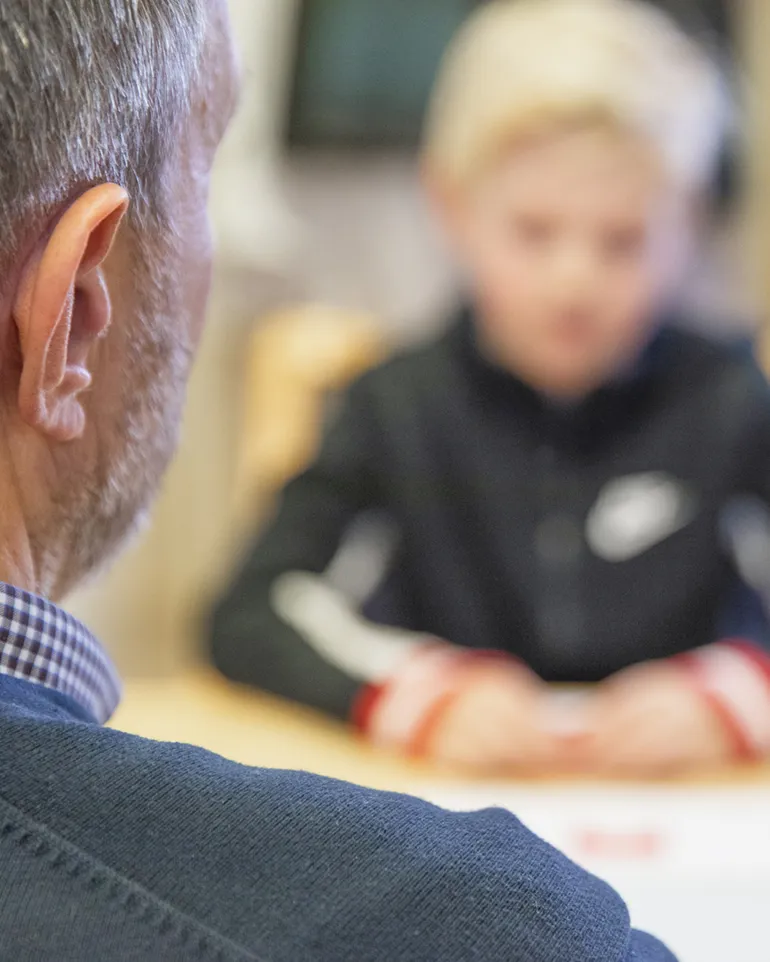 En gutt sitter ved et bord med en voksen mann på andre siden av bordet.