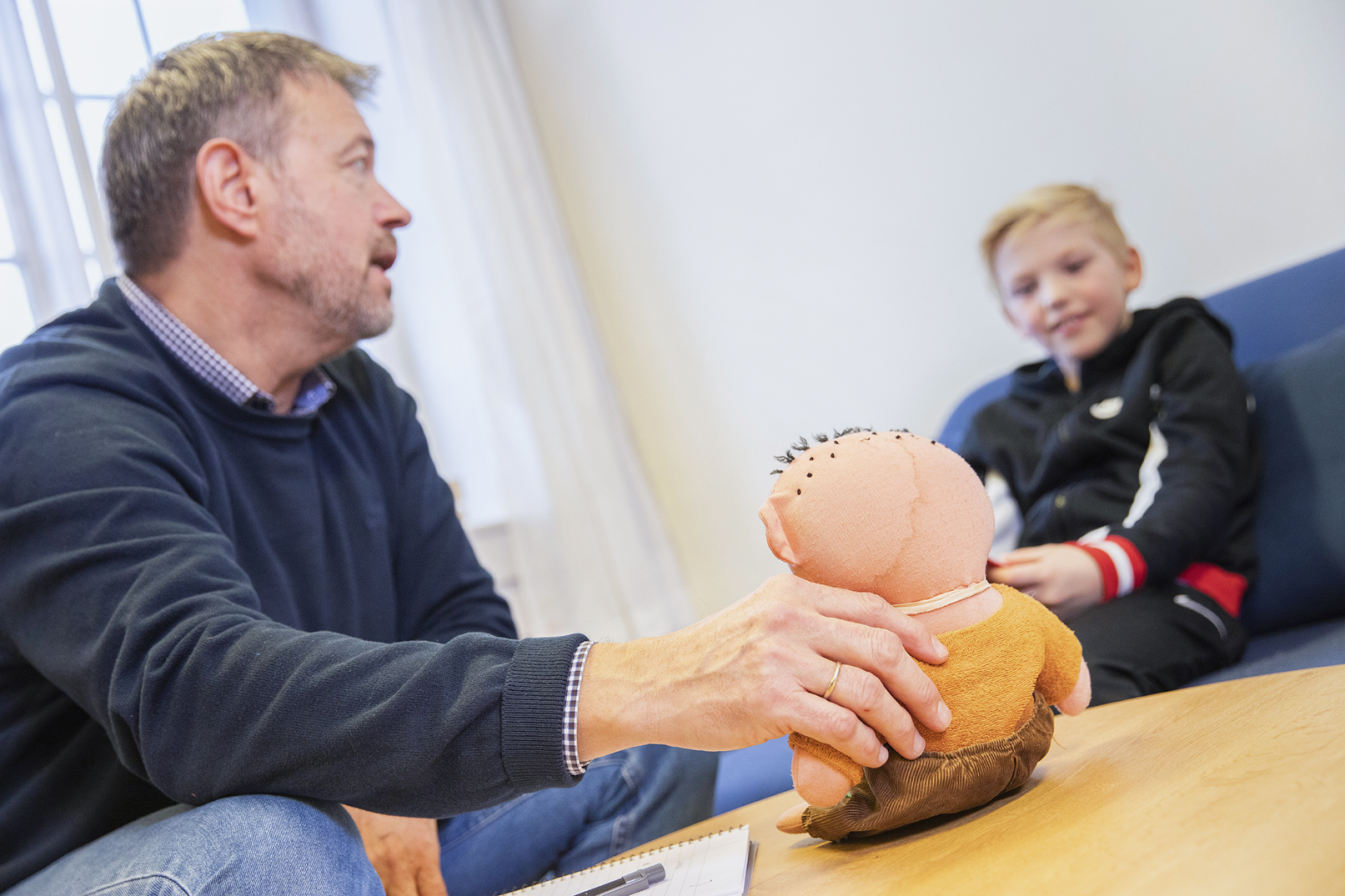 Et barn, en behandler og en liten bamse.