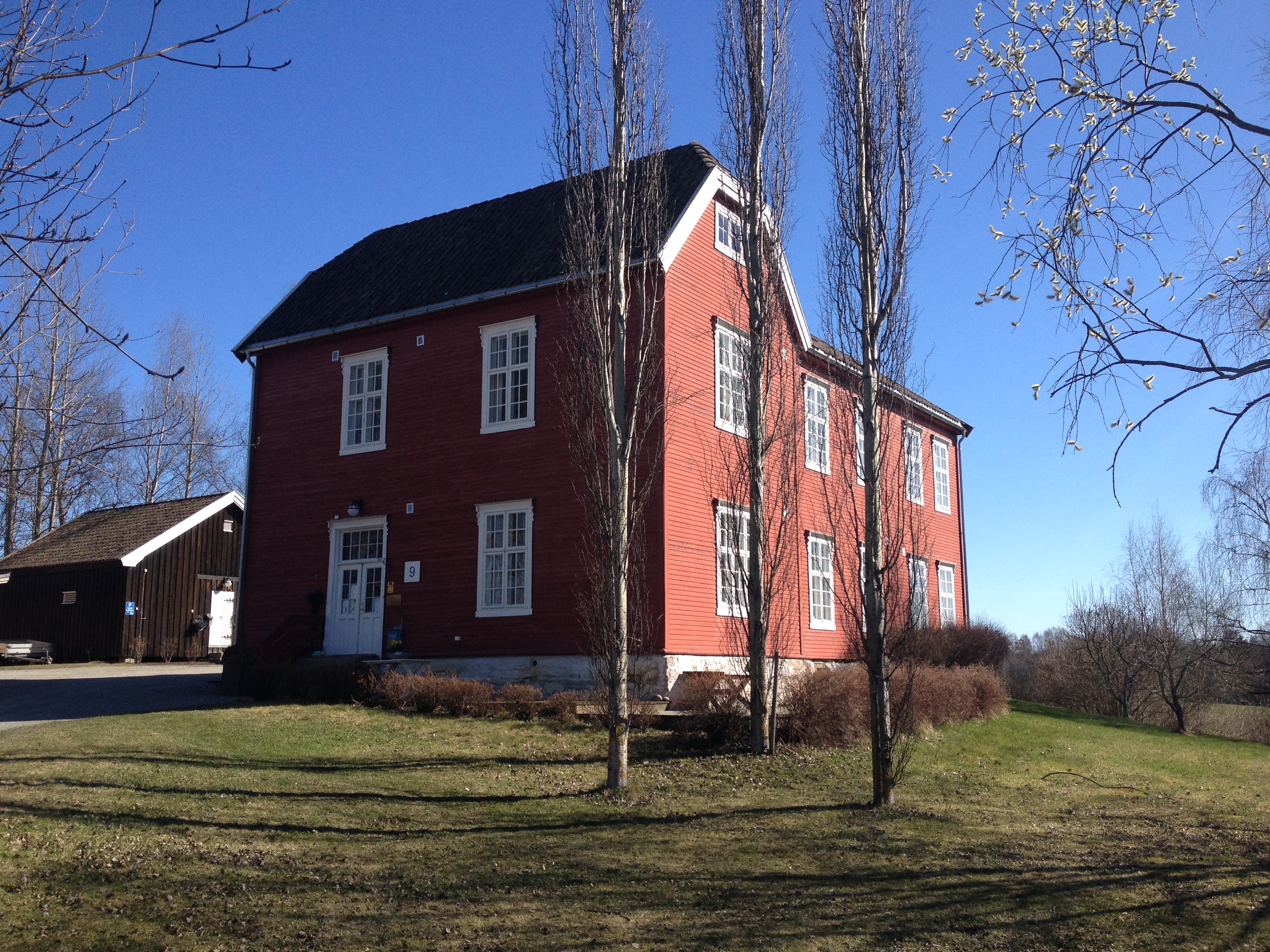 Blaarud aktivitetshus, rødt hus med hvitmalte vinduer omgitt av hage med grønt gress, hekk og trær