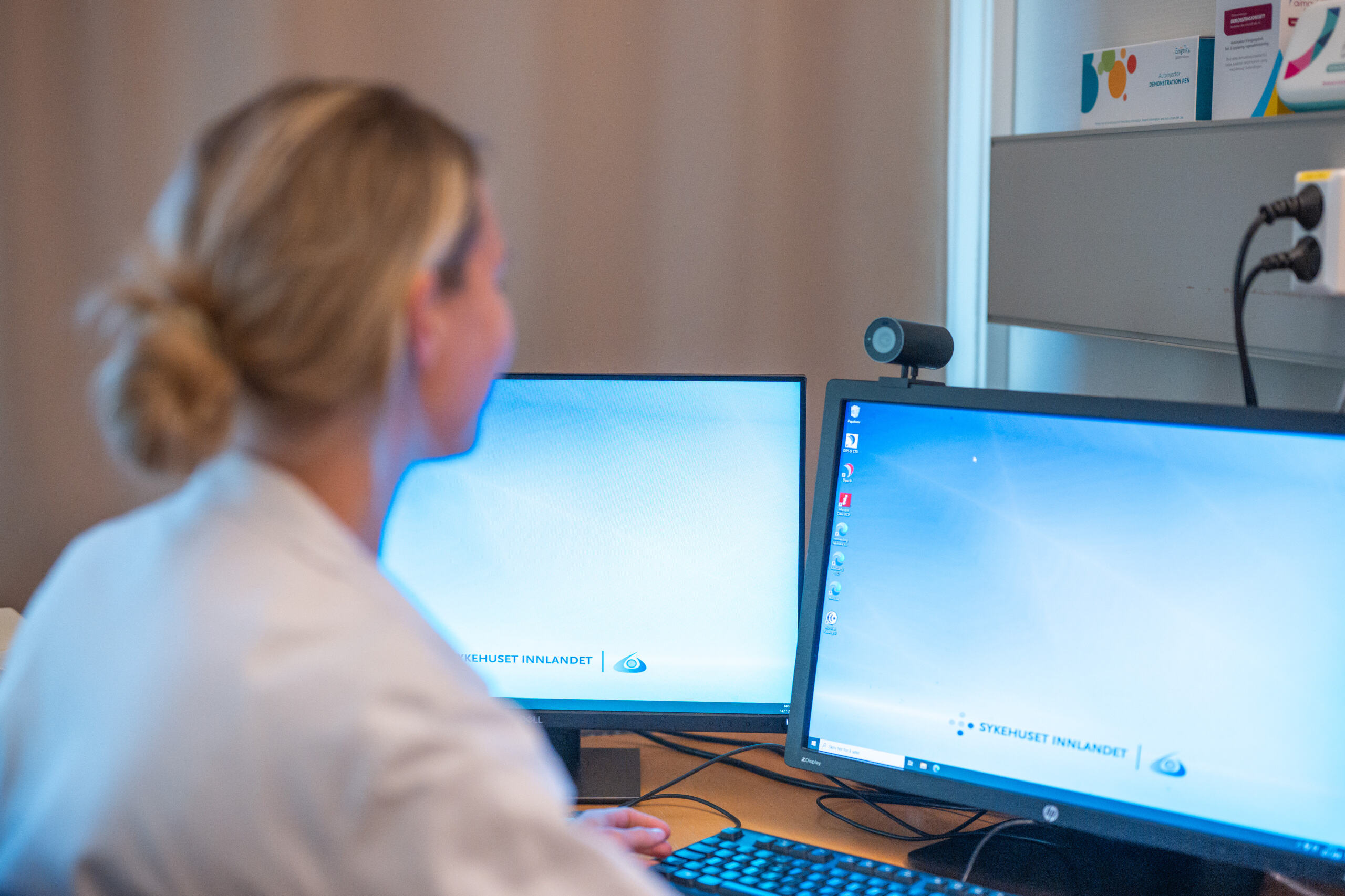 Helsepersonell i hvitt sitter foran to skjerme