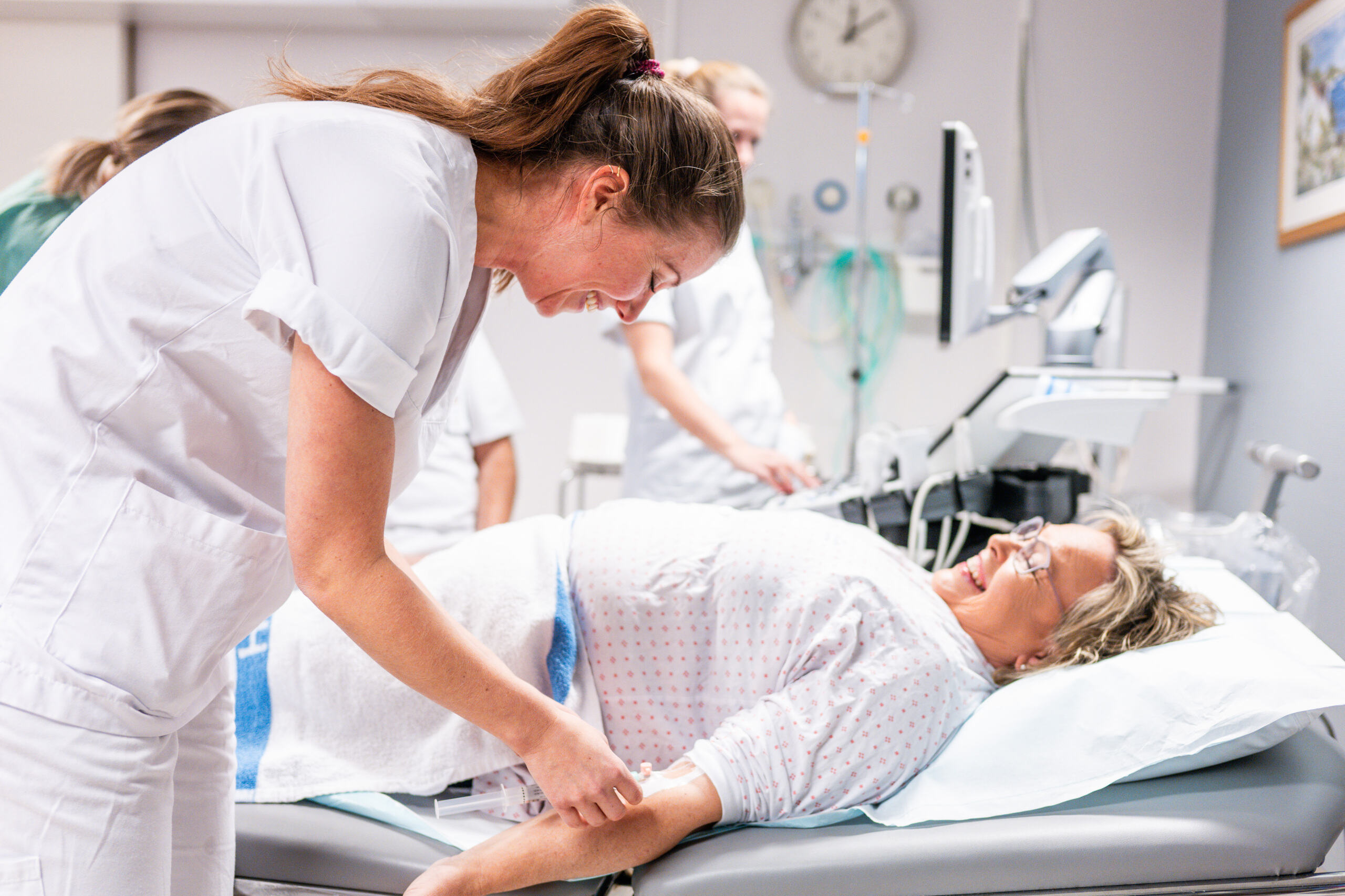 En pasient ligger i seng mens helsepersonell jobber rundt sengen.