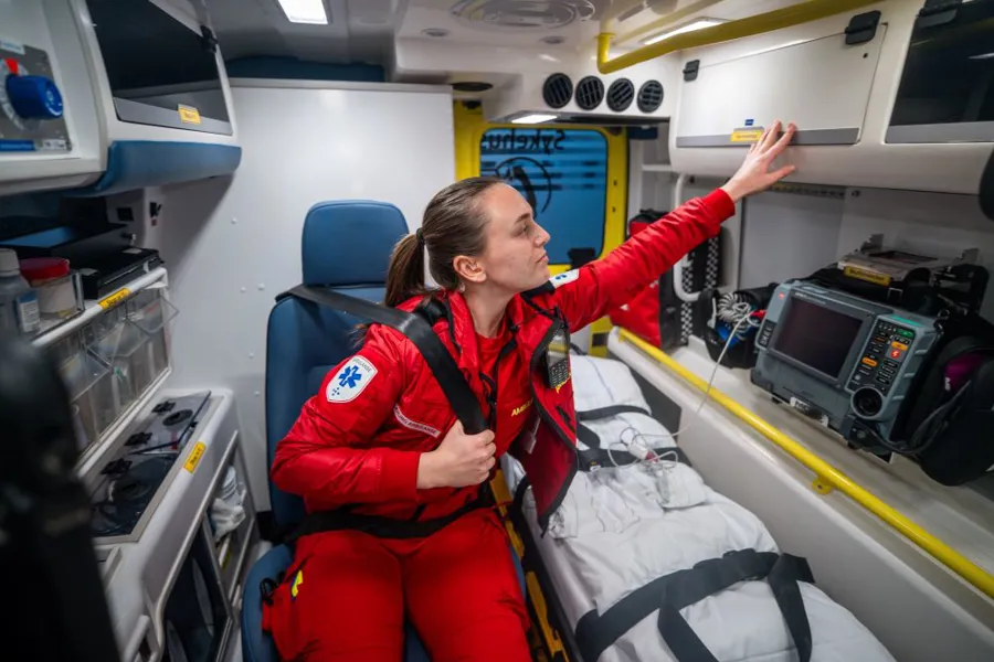 Lærling i røde ambulanseklær på jobb i ambulansen.