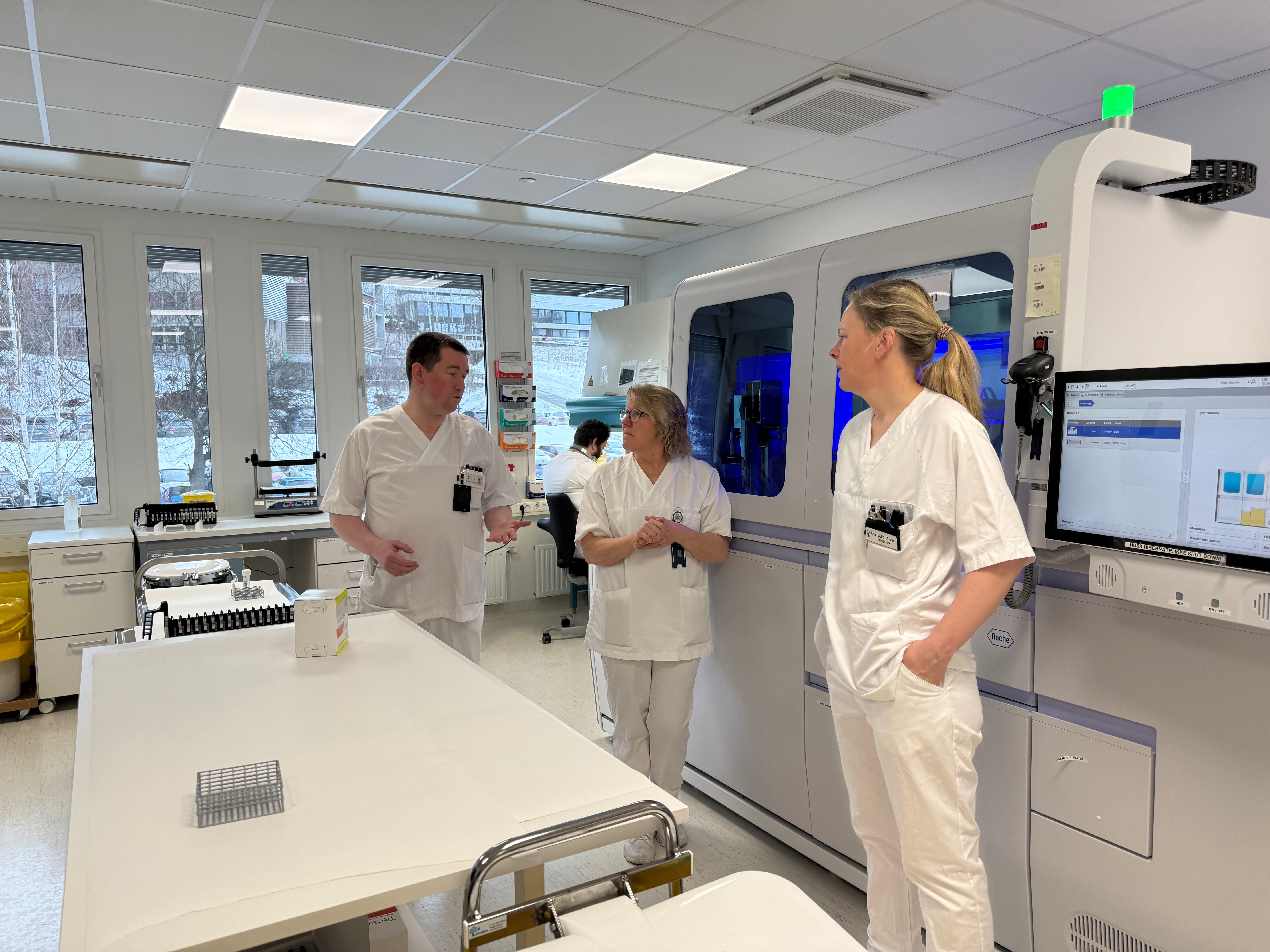 En gruppe mennesker i hvite laboratoriefrakker i et rom med en datamaskin