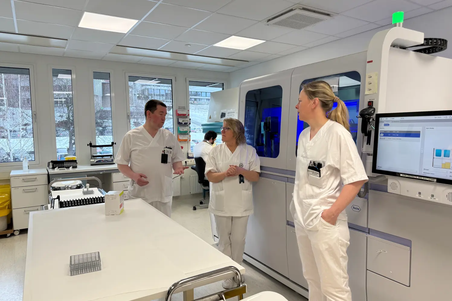 En gruppe mennesker i hvite laboratoriefrakker i et rom med en datamaskin