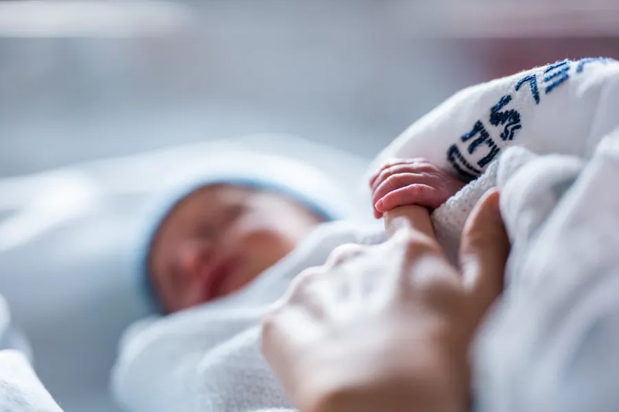 Et nærbilde av en nyfødt baby som holder hånden rundt en voksen finger.