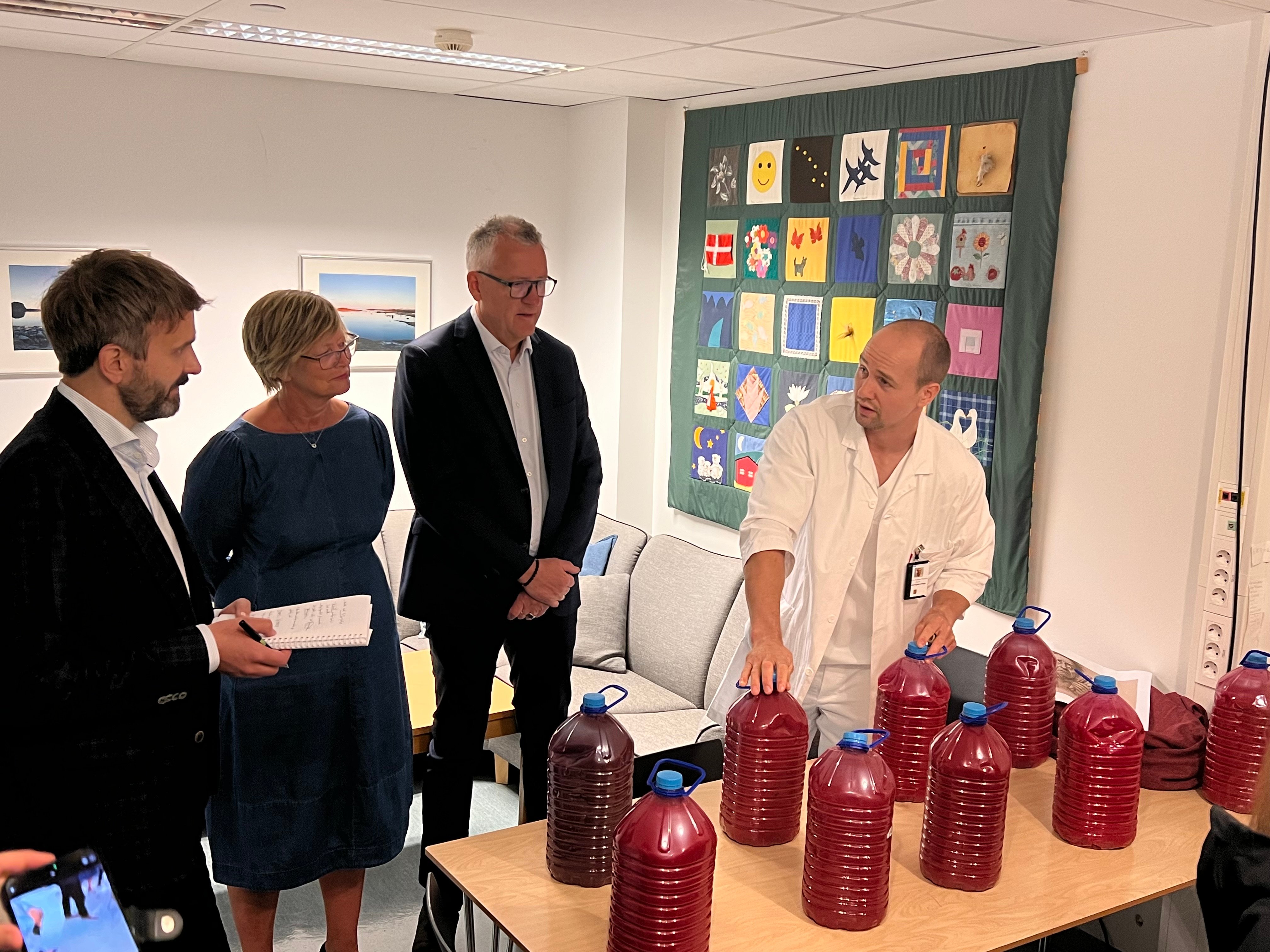 En gruppe mennesker som står rundt et bord med krukker med rød væske