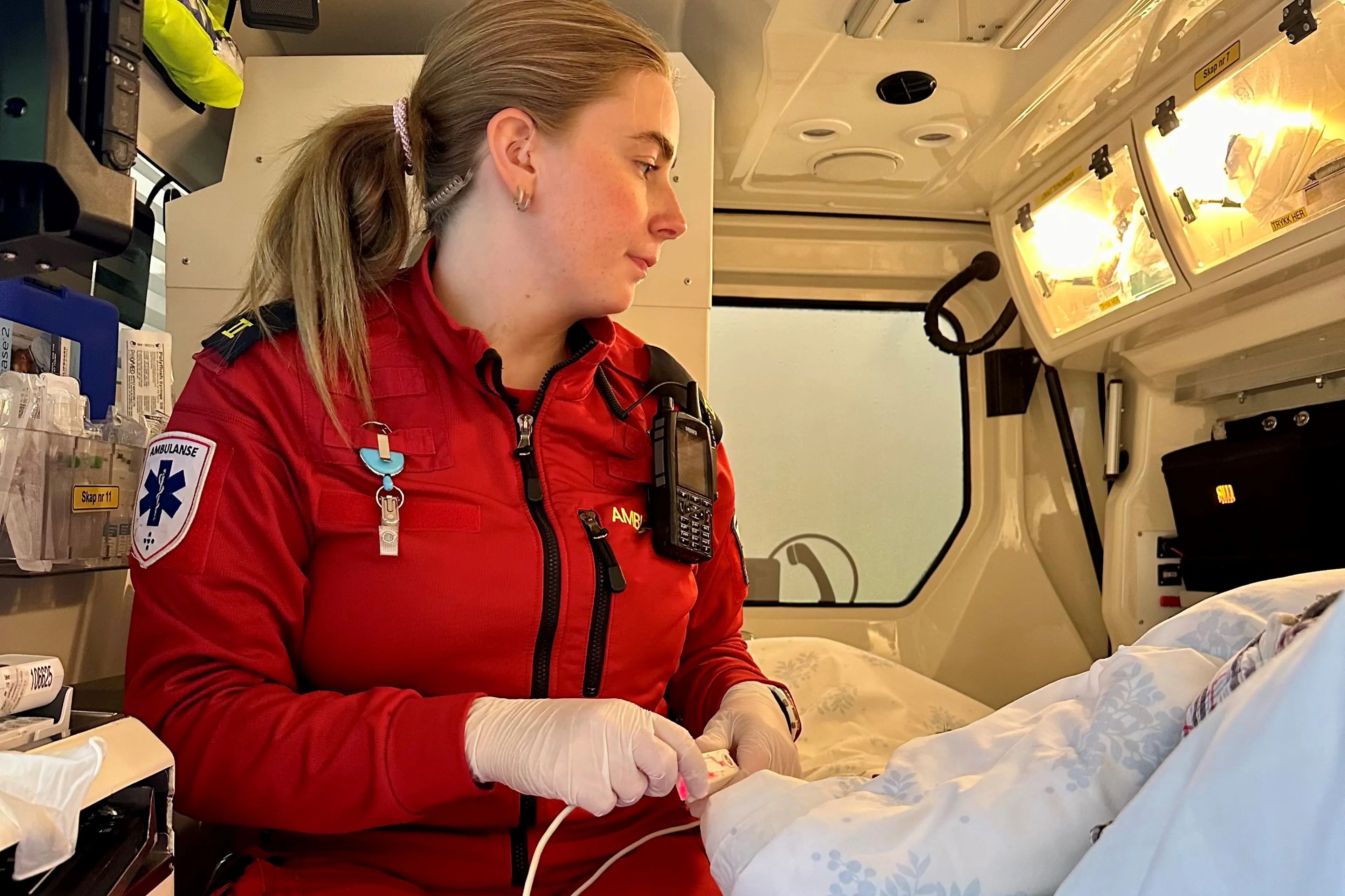 En person i rød frakk som holder en baby i en sykehusseng
