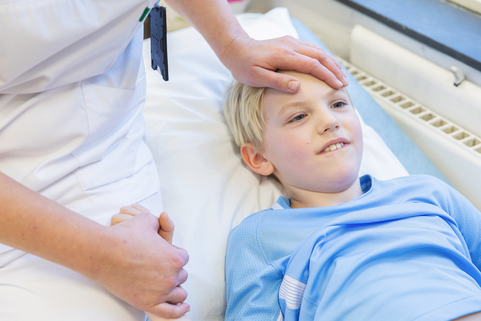 Sykepleier holder et barn i sykehusseng i hånda.