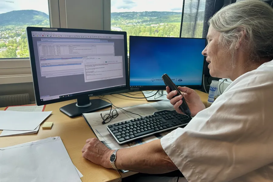 Avdelingsoverlege Ellen Bøhmer sitter ved datamaskin og bruker utstyr for talegjenkjenning