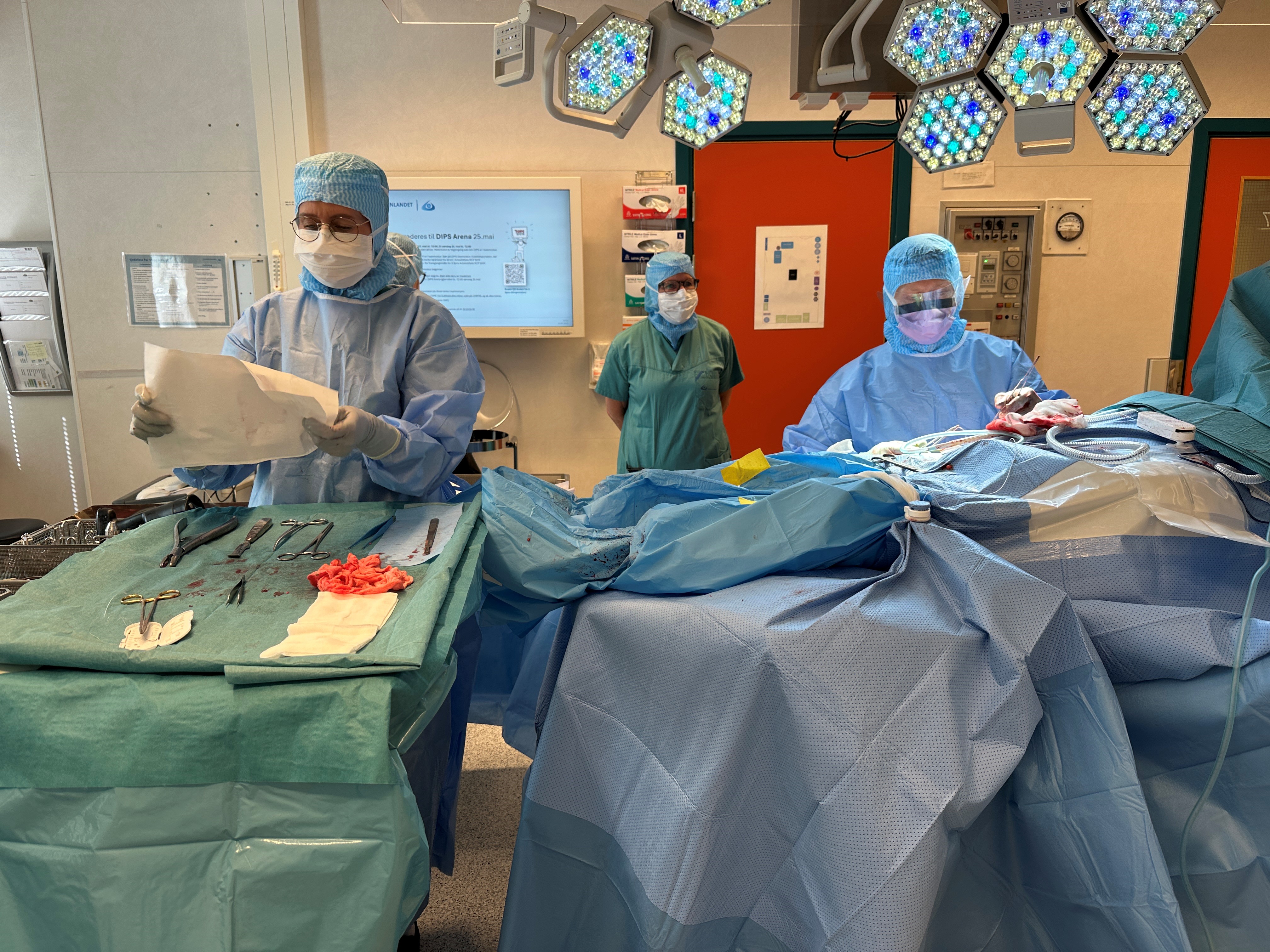 En gruppe mennesker i kirurgiske skrubb som jobber med en pasient