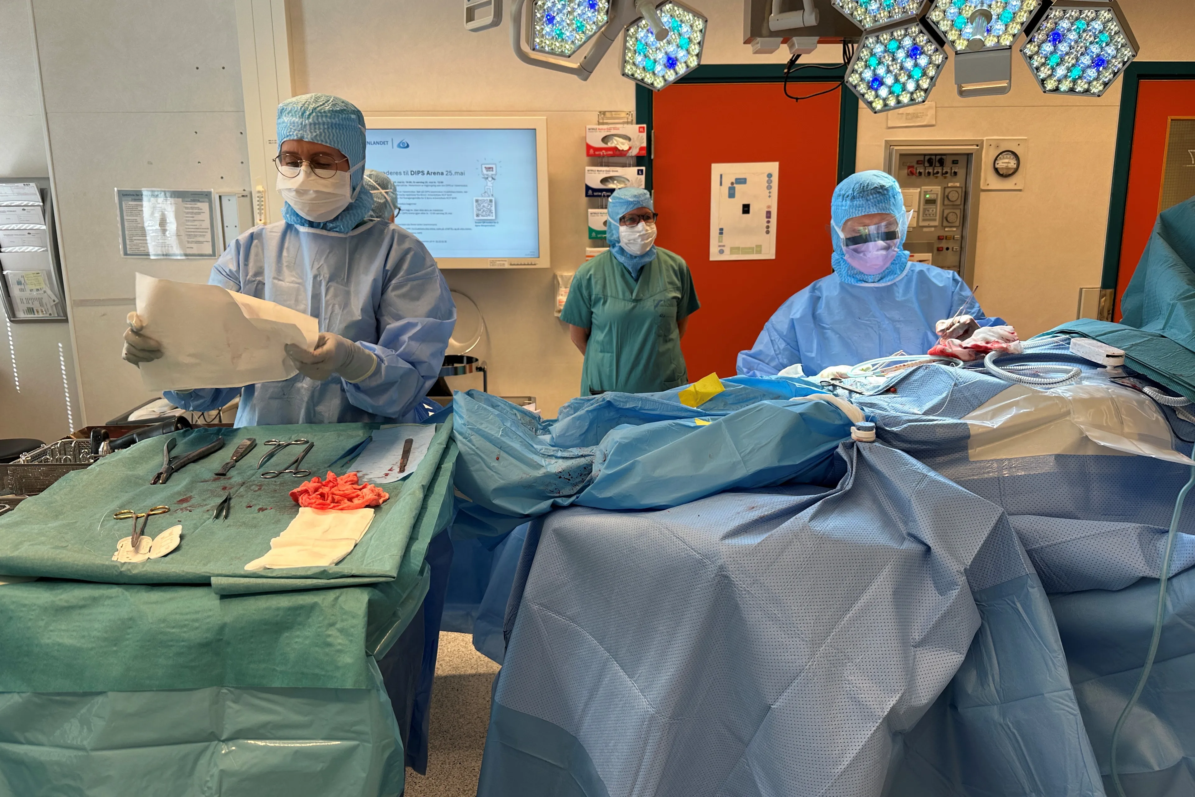 En gruppe mennesker i kirurgiske skrubb som jobber med en pasient