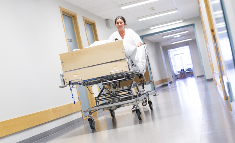 Sykepleier triller en sykehusseng i korridor.