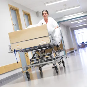 Sykepleier triller en sykehusseng i korridor.
