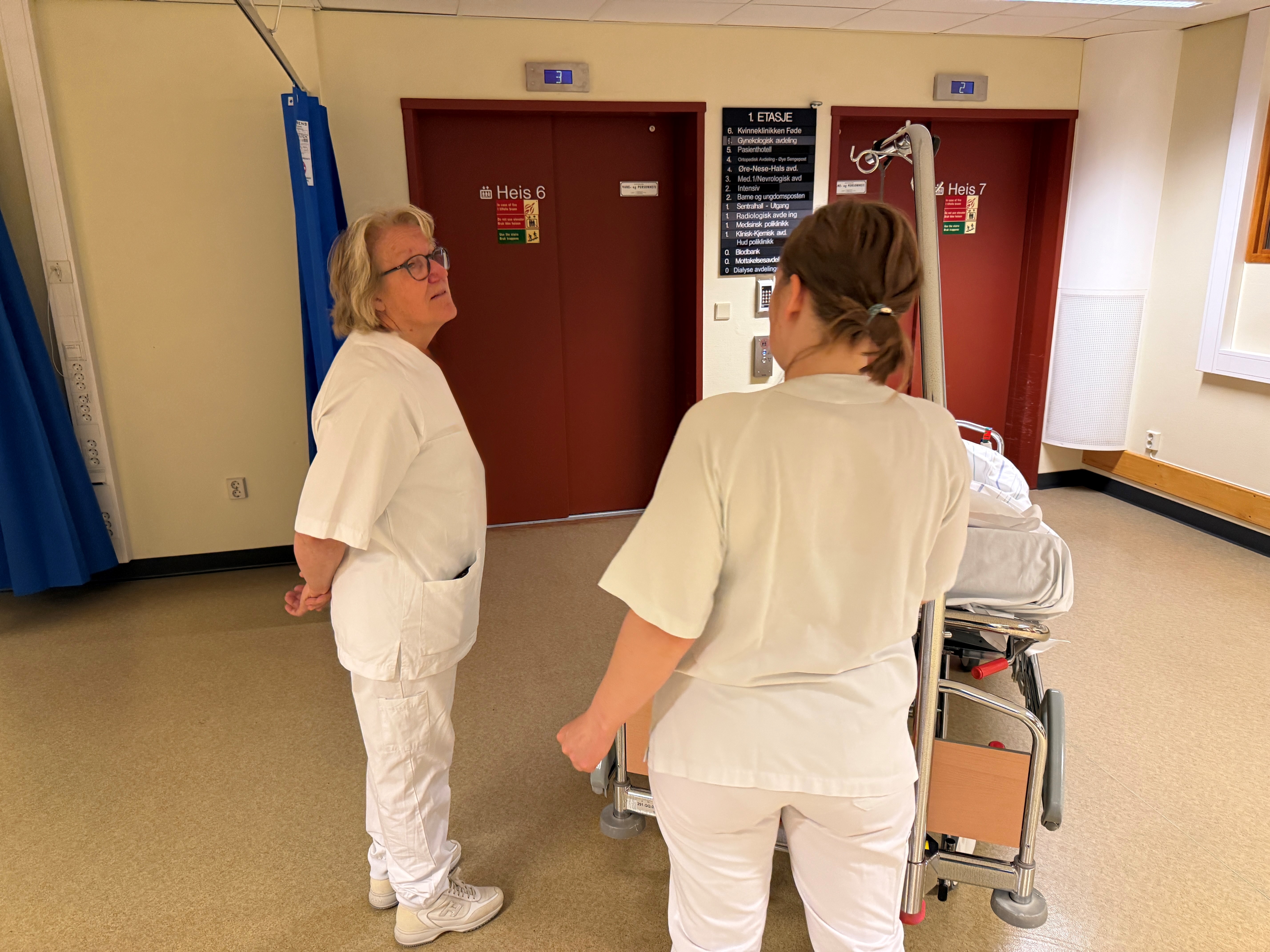 Hospitant og portør med pasient i seng foran heis