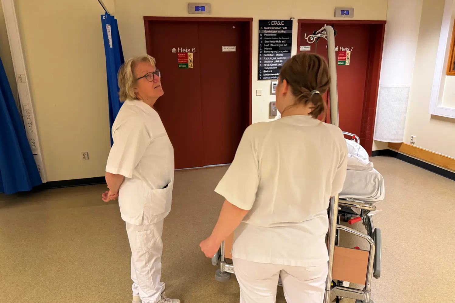 Hospitant og portør med pasient i seng foran heis
