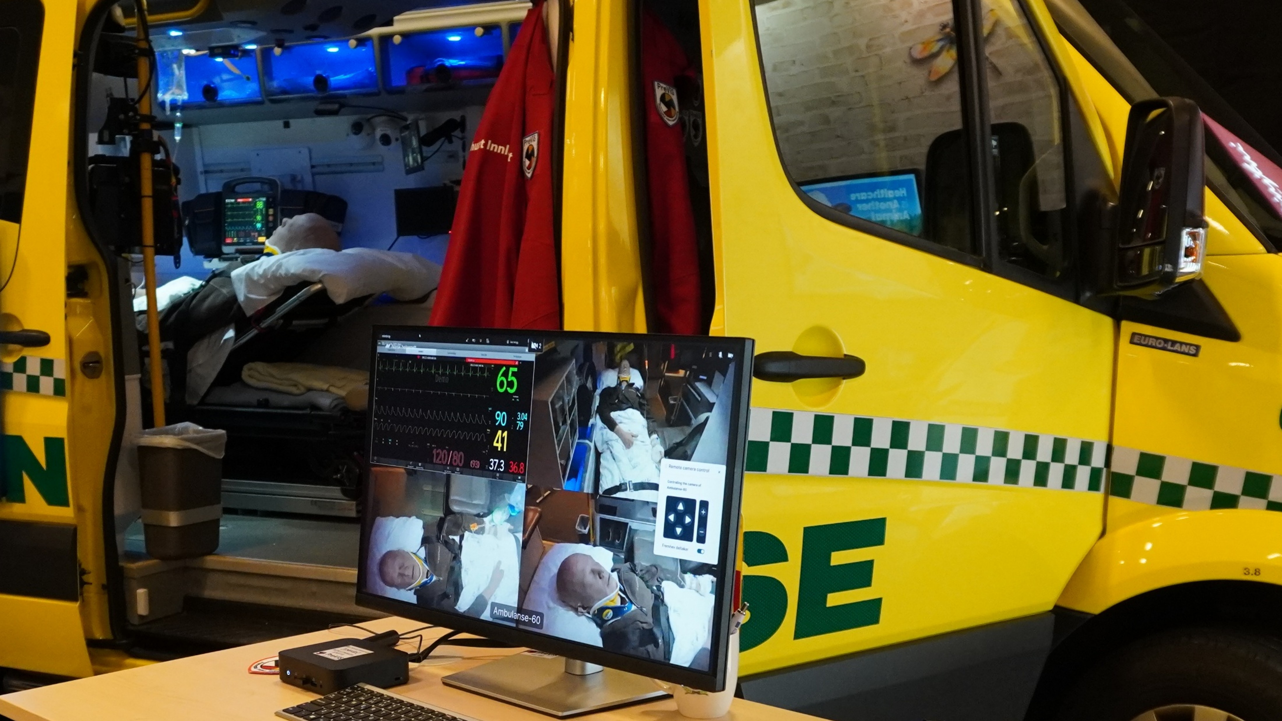 Gul ambulanse med en person liggende på båre og en skjerm
