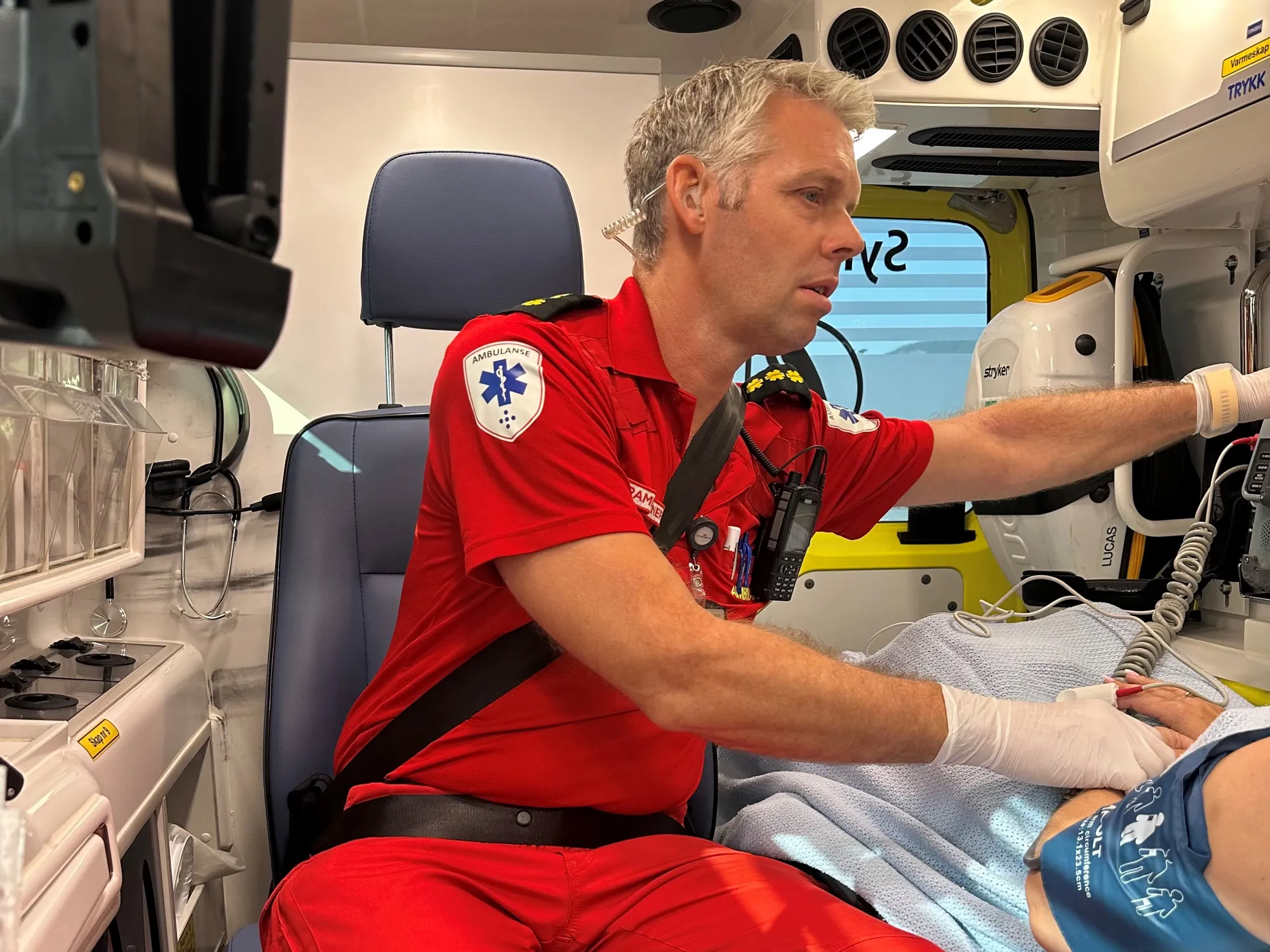 Ambulansearbeider behandler pasient under ambulansetransport.