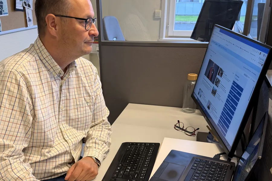 En mann som sitter ved et skrivebord med en datamaskin og en bærbar PC