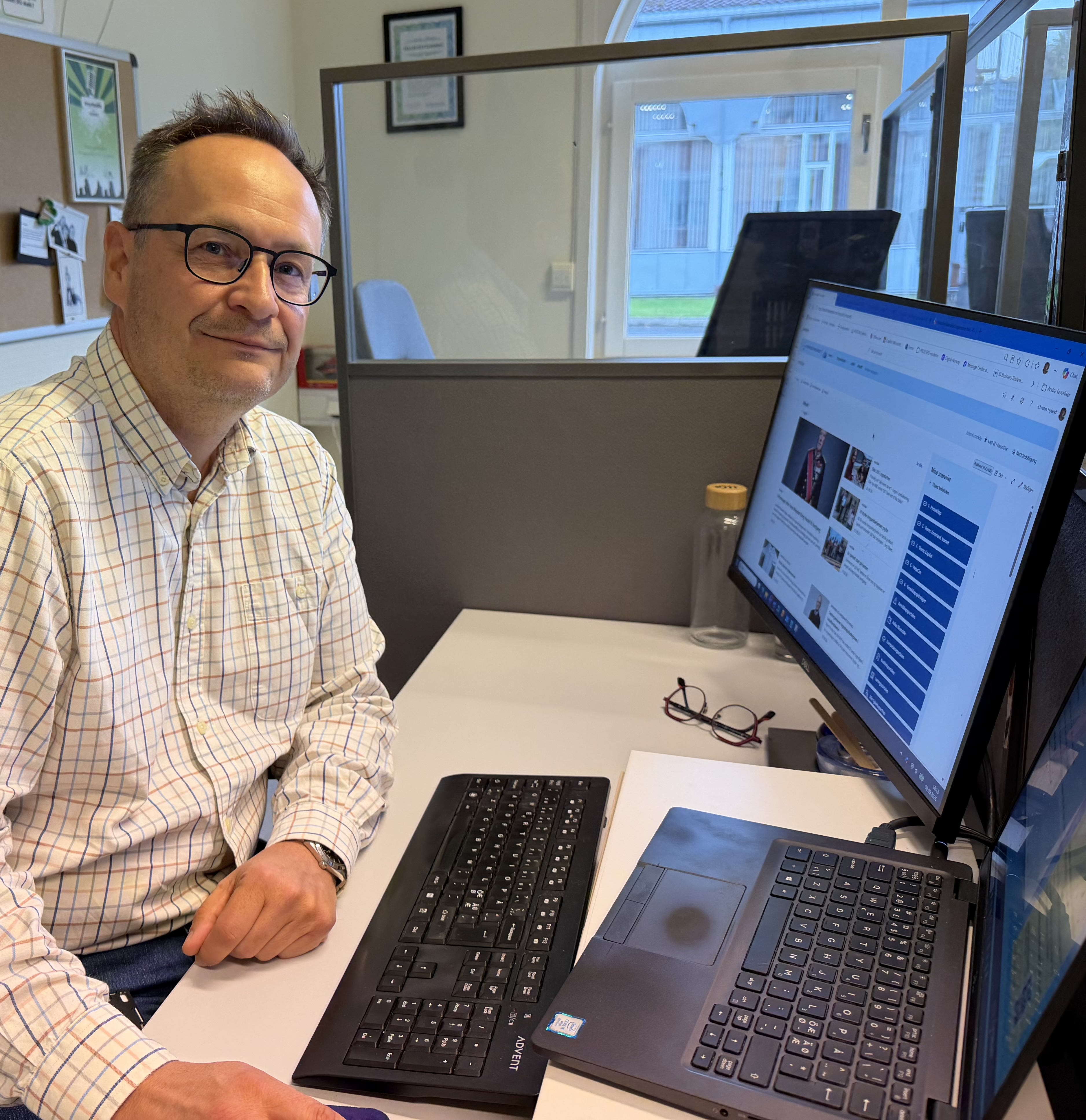 En mann som sitter ved et skrivebord med en laptop og en datamaskin