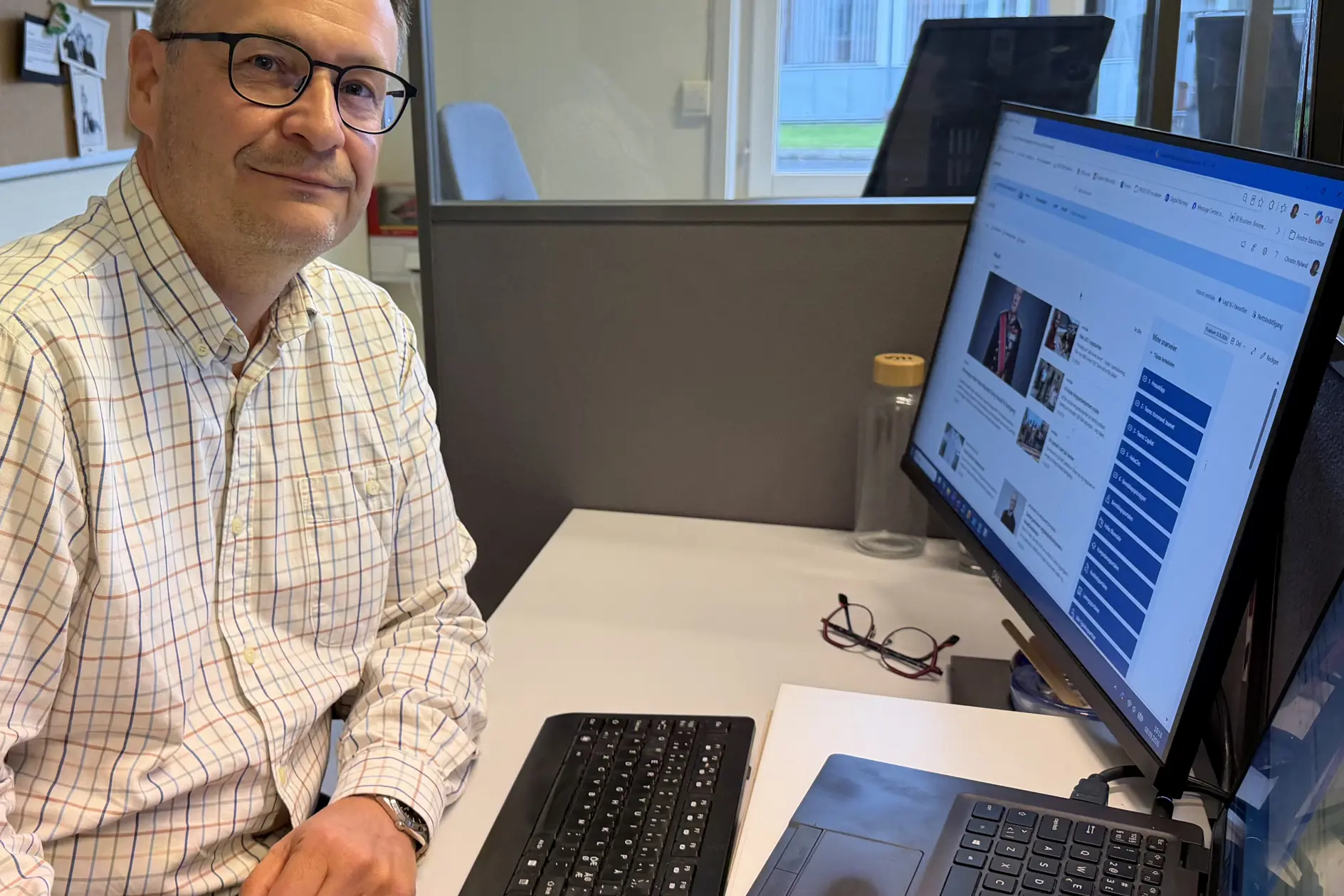 En mann som sitter ved et skrivebord med en laptop og en datamaskin