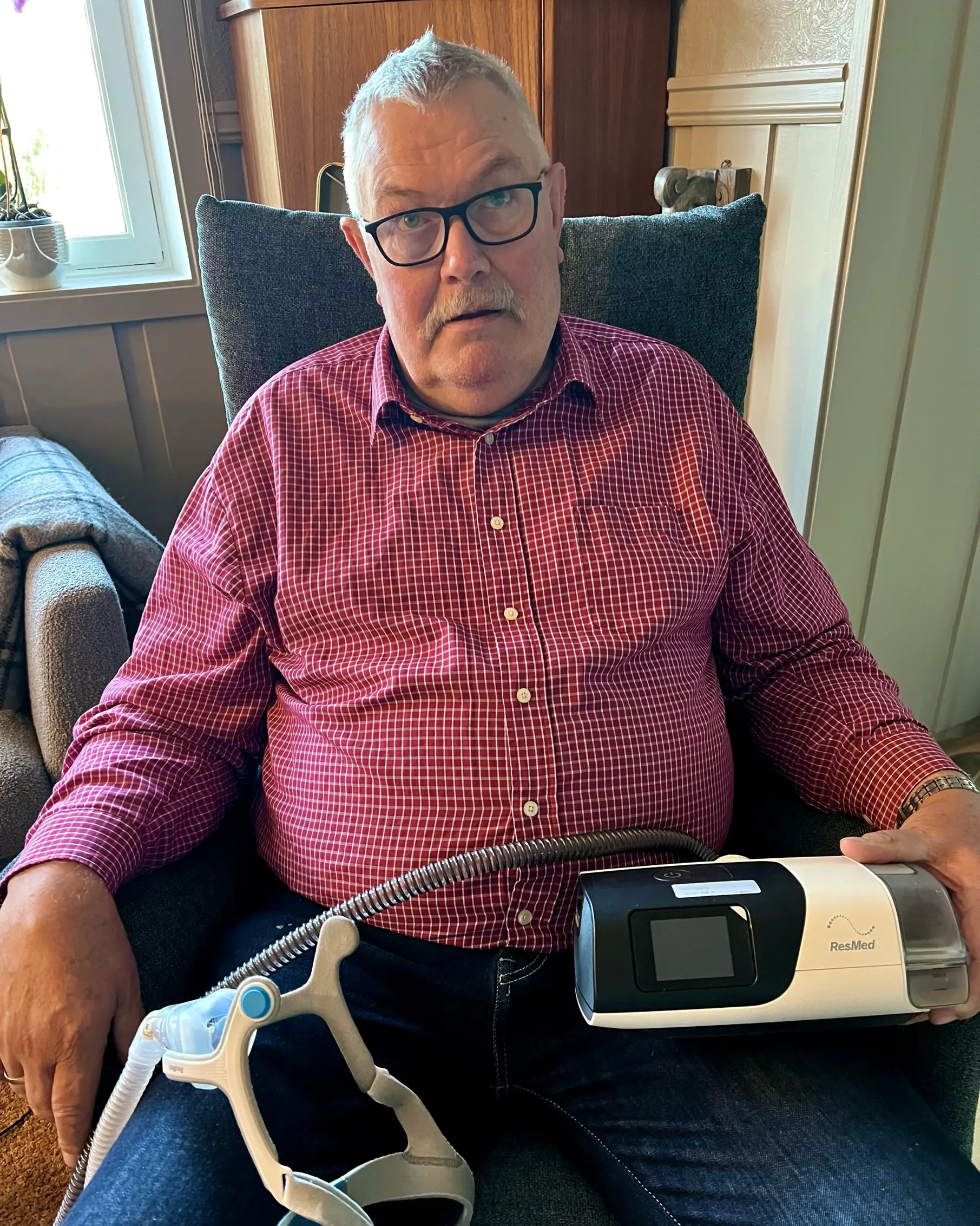 Søvnapnépasient Tom Gaustad sitter og holder sitt CPAP-apparat