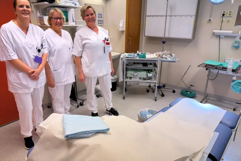 En gruppe kvinner i hvite laboratoriefrakker som står ved siden av en pasient