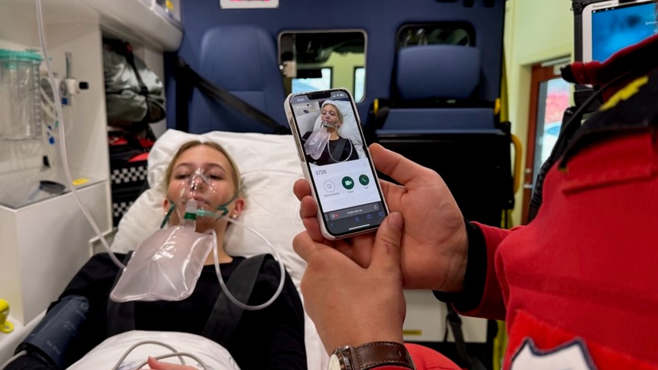 Ambulansearbeider med mobil i hånda filmer pasient på båre