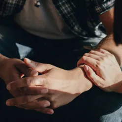 Mann folder hender, med hånden til dame på låret.