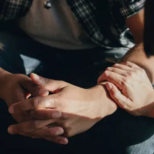 Mann folder hender, med hånden til dame på låret.