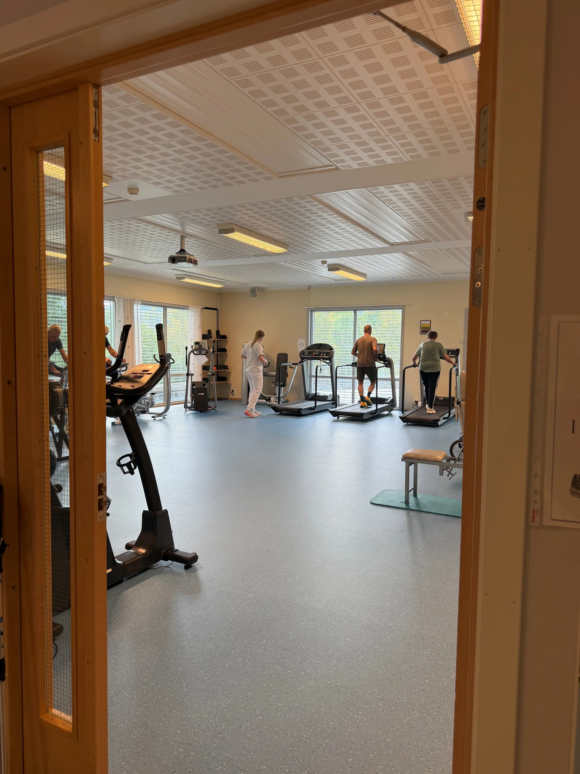 Ser gjennom døra og inn i et treningsrom med personer som jobber på tredemølle