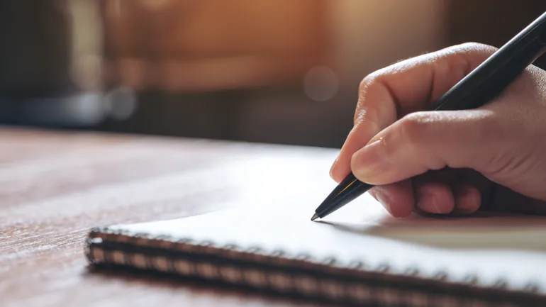 Hånd som holder en skriveblyant mot en skriveblokk.