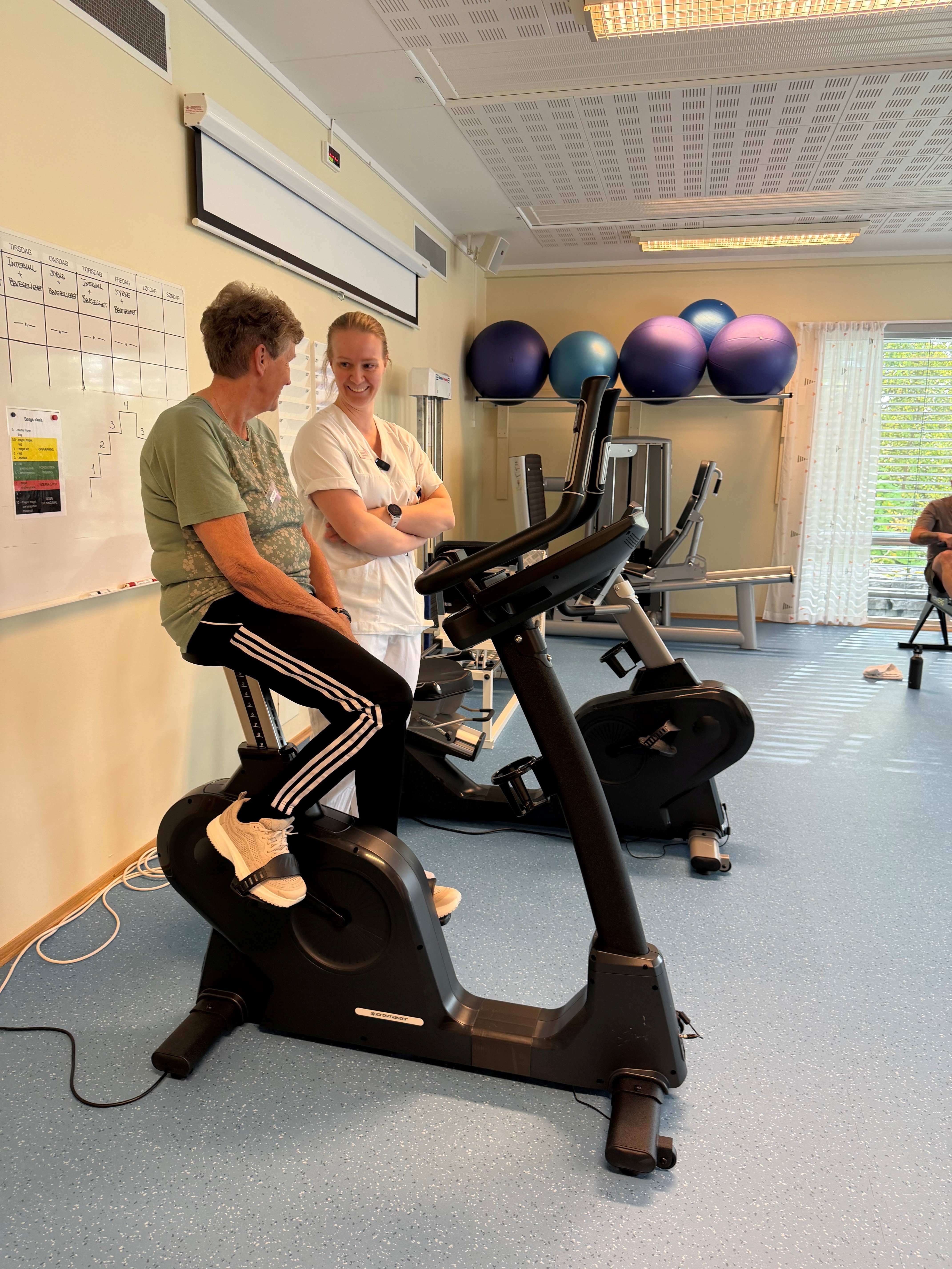 Kvinne på ergometersykkel og helsepersonell følger med.