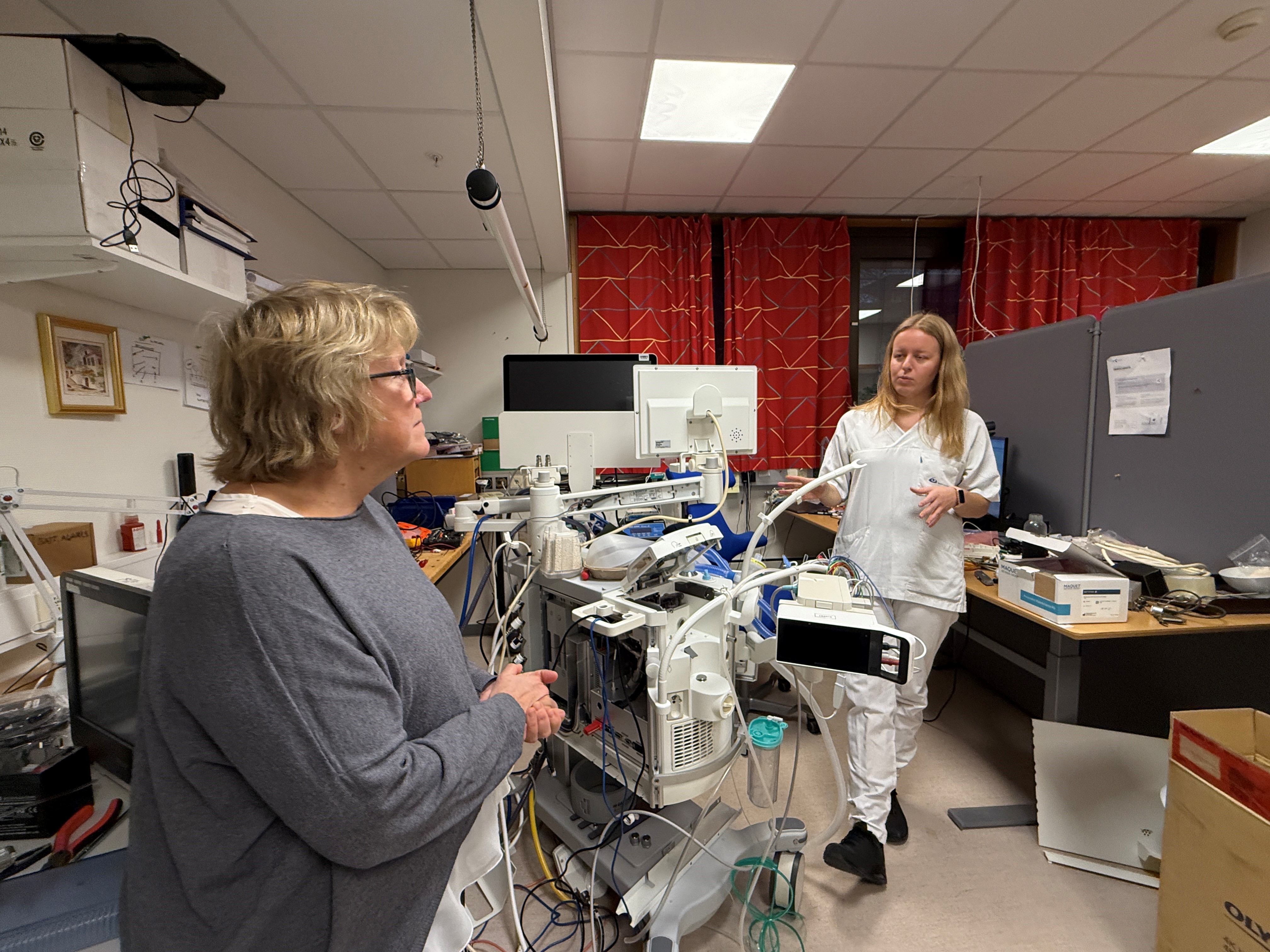 En person som står ved siden av en person i et rom med datamaskiner