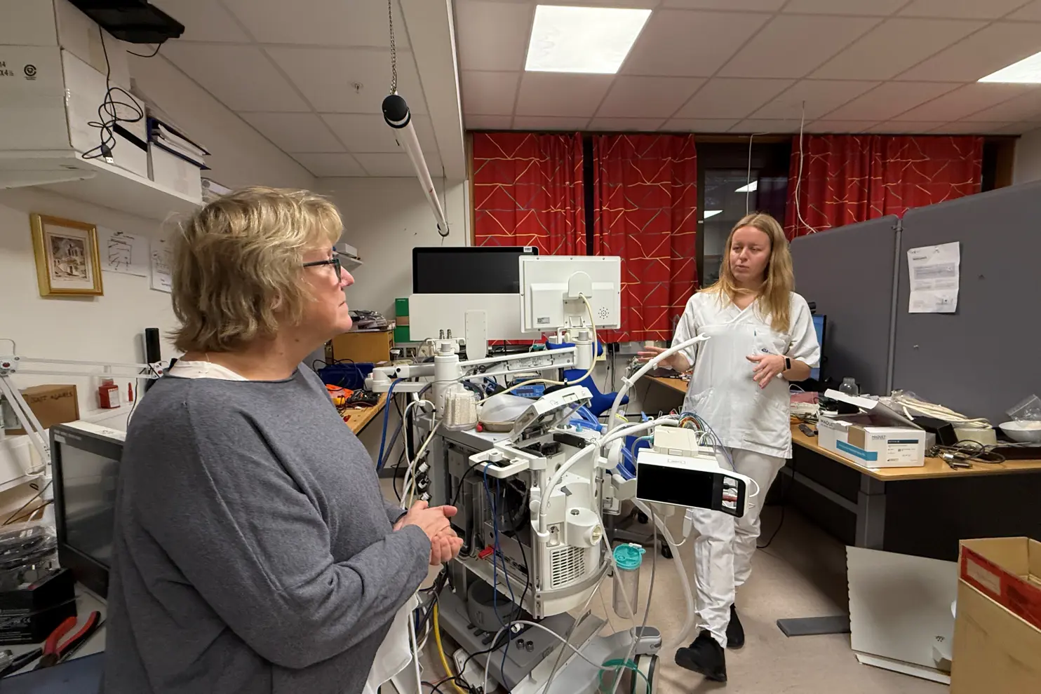 En person som står ved siden av en person i et rom med datamaskiner