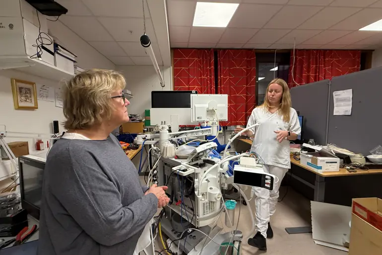 En person som står ved siden av en person i et rom med datamaskiner